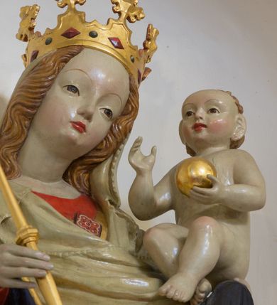Zdjęcie nr 7: Rzeźba pełnoplastyczna, wolnostojąca, ukazująca Matkę Boską z Dzieciątkiem. Maria ustawiona frontalnie, w kontrapoście o sylwetce wygiętej na kształt litery „S”, z głową przechyloną na lewo. Na lewym ręku trzyma Dzieciątko i podtrzymuje dłonią płaszcz, w prawej dzierży berło. Twarz okrągła z wysokim czołem, drobnymi ustami i małymi oczami, o delikatnie zarysowanych łukach brwiowych. Włosy jasne, ułożone w skręcone pukle spływające na plecy. Madonna ubrana jest w czerwoną suknię, złoty płaszcz z ciemnogranatową podszewką spięty na piersi broszą w kształcie rombu oraz czarne buty. Na głowie ma założony beżowy welon spływający na ramiona i piersi oraz złotą koronę w typie otwartym, kameryzowaną. Draperia szat miękka o wyraźnie zaznaczonych, licznych fałdach misowych i kaskadowych. Dzieciątko ukazane w pozycji siedzącej, zwrócone w prawo, z nóżkami skrzyżowanymi, założonymi lewa na prawą. W lewej dłoni trzyma jabłko królewskie, a prawą podnosi do gestu błogosławieństwa. Twarz o dziecięcych rysach, z wysokim i wypukłym czołem, z delikatnie otwartymi ustami, okolona krótkimi i kędzierzawymi włosami. Polichromia w odsłoniętych partiach ciała o delikatnych odcieniach szarości, płaszcz i atrybuty złocone. 