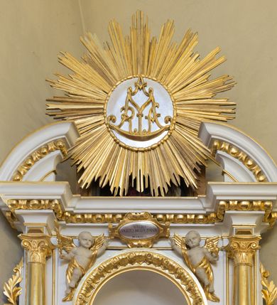 Zdjęcie nr 2: Ołtarz drewniany, prostopadłościenny, na jednostopniowej podstawie. Mensa drewniana z portatylem z marmuru dębnickiego z kwadratowym reservaculum na relikwie św. Konstancji i św. Teodora. Antepedium w formie leżącego  prostokąta ujętego grubą ramą, dekorowaną płaskorzeźbionym akantem. W polu, w centrum malowany na desce rollwerk z monogramem Marii w polu, ujęty wolutami utworzonymi z ornamentu roślinnego o wici zakończonej kampanulą. Tabernakulum w formie prostopadłościennej skrzynki o delikatnie wypukłej ściance frontowej. Całość zamknięta opasującym je z trzech stron gzymsem przyjmującym nad polem środkowym kształt łuku segmentowego podtrzymywanego przez dwie konsole utworzone z akantu. Drzwiczki w kształcie stojącego prostokąta zamkniętego łukiem półkolistym nadwieszonym, ujęte ramą. W polu ryte przedstawienie kielicha z hostią. Tabernakulum flankowane spływami wolutowymi utworzonymi z akantu. Nastawa ołtarzowa architektoniczna, jednoosiowa, jednokondygnacyjna ze zwieńczeniem, na niewielkim cokole. Kondygnacja ujęta parą kolumn o kapitelach kompozytowych dźwigających pełne belkowanie wyłamane na ich osi oraz przerwany półkolisty przyczółek. W polu środkowym nisza w formie stojącego prostokąta zamkniętego łukiem półkolistym, ujęta ramą z figurą Matki Boskiej z Dzieciątkiem. Zwieńczenie w formie medalionu z płaskorzeźbionym monogramem Marii w glorii promienistej. W przyłuczach niszy w polu środkowym para puttów podtrzymujących owalny kartusz z napisem w polu „WIELBIJ / DUSZO MOJA PANA / ŚW(IĘTY) ŁUKASZ I R(OZDZIAŁ)”. Kondygnacja flankowana uszami utworzonymi z suchego akantu. Gzyms oraz przerwany przyczółek dekorowane kimationem. Struktura polichromowana w kolorze białym, ornamentyka, profile i kolumny złocone.
