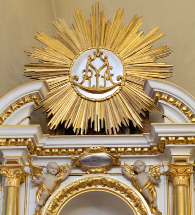 Zdjęcie nr 8: Ołtarz drewniany, prostopadłościenny, na jednostopniowej podstawie. Mensa drewniana z portatylem z marmuru dębnickiego z kwadratowym reservaculum na relikwie św. Konstancji i św. Teodora. Antepedium w formie leżącego  prostokąta ujętego grubą ramą, dekorowaną płaskorzeźbionym akantem. W polu, w centrum malowany na desce rollwerk z monogramem Marii w polu, ujęty wolutami utworzonymi z ornamentu roślinnego o wici zakończonej kampanulą. Tabernakulum w formie prostopadłościennej skrzynki o delikatnie wypukłej ściance frontowej. Całość zamknięta opasującym je z trzech stron gzymsem przyjmującym nad polem środkowym kształt łuku segmentowego podtrzymywanego przez dwie konsole utworzone z akantu. Drzwiczki w kształcie stojącego prostokąta zamkniętego łukiem półkolistym nadwieszonym, ujęte ramą. W polu ryte przedstawienie kielicha z hostią. Tabernakulum flankowane spływami wolutowymi utworzonymi z akantu. Nastawa ołtarzowa architektoniczna, jednoosiowa, jednokondygnacyjna ze zwieńczeniem, na niewielkim cokole. Kondygnacja ujęta parą kolumn o kapitelach kompozytowych dźwigających pełne belkowanie wyłamane na ich osi oraz przerwany półkolisty przyczółek. W polu środkowym nisza w formie stojącego prostokąta zamkniętego łukiem półkolistym, ujęta ramą z figurą Matki Boskiej z Dzieciątkiem. Zwieńczenie w formie medalionu z płaskorzeźbionym monogramem Marii w glorii promienistej. W przyłuczach niszy w polu środkowym para puttów podtrzymujących owalny kartusz z napisem w polu „WIELBIJ / DUSZO MOJA PANA / ŚW(IĘTY) ŁUKASZ I R(OZDZIAŁ)”. Kondygnacja flankowana uszami utworzonymi z suchego akantu. Gzyms oraz przerwany przyczółek dekorowane kimationem. Struktura polichromowana w kolorze białym, ornamentyka, profile i kolumny złocone.
