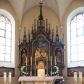 Zdjęcie nr 1: Nastawa ołtarzowa architektoniczna, jednokondygnacyjna, trójosiowa. Ołtarz kamienny, prostopadłościenny, ustawiony na dwustopniowej podstawie. Mensa kamienna, silnie wysunięta, podtrzymywana przez dwie kamienne kolumienki. Antepedium podzielone na trzy kwadratowe pola z płycinami, w środkowej wysuniętej do przodu medalion z monogramem IHS w polu. Tabernakulum w formie prostopadłościennej skrzynki, obitej fakturowaną blachą, od frontu ujęte parą kolumienek. Drzwiczki w kształcie stojącego prostokąta, dwuskrzydłowe z trybowanym przedstawieniem kielicha z unoszącą się Hostią w glorii, adorowaną przez dwa klęczące anioły. Tron do wystawiania monstrancji w formie baldachimu podtrzymywanego przez cztery kolumienki oraz z zabudowaną ścianką tylną dekorowaną rytym wzorem z czteroliści i medalionu z monogramem IHS w glorii podtrzymywanym przez parę unoszących się aniołów. Baldachim w formie dwuspadowego daszku zwieńczonego pseudowieżyczką z krzyżem; od frontu zamknięty wimpergą. Nastawa ołtarzowa ustawiona na dwustrefowym cokole z predellą dekorowaną blendami. Osie wydzielone czterema kolumnami dźwigającymi pinakle. Oś środkowa, najszersza ujęta dwiema dwustrefowymi płytkimi niszami zakończonymi trójlistnie z półpełnymi figurkami świętych: Dominika i Izydora po prawej oraz Ambrożego i Jacka po lewej; zwieńczona wimpergą, flankowaną przez dwie figurki aniołków nakryte baldachimami w formie sterczyn. W polu nisza w formie stojącego prostokąta zamkniętego łukiem trójlistnym z płaskorzeźbionym przedstawieniem Trójcy Świętej. Osie boczne z niszami w formie stojącego prostokąta zamkniętego łukiem półkolistym z figurami św. Wojciecha (po lewej) i św. Stanisława (po prawej), zamknięte dwiema wimpergami ze sterczynami oraz jednospadowym daszkiem z ażurową wieżyczką. Zwieńczenie w formie ażurowej wieżyczki z figurką św. Józefa z Dzieciątkiem, zakończonej dużą sterczyną z krzyżem dekorowaną żabkami. Struktura w kolorze naturalnego drewna, profile i ornamentyka złocone, tło pola środkowego w kolorze błękitnym, detale zielone.
