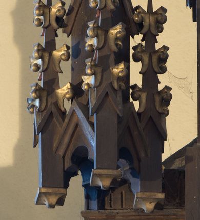 Zdjęcie nr 10: Nastawa ołtarzowa architektoniczna, jednokondygnacyjna, trójosiowa. Ołtarz kamienny, prostopadłościenny, ustawiony na dwustopniowej podstawie. Mensa kamienna, silnie wysunięta, podtrzymywana przez dwie kamienne kolumienki. Antepedium podzielone na trzy kwadratowe pola z płycinami, w środkowej wysuniętej do przodu medalion z monogramem IHS w polu. Tabernakulum w formie prostopadłościennej skrzynki, obitej fakturowaną blachą, od frontu ujęte parą kolumienek. Drzwiczki w kształcie stojącego prostokąta, dwuskrzydłowe z trybowanym przedstawieniem kielicha z unoszącą się Hostią w glorii, adorowaną przez dwa klęczące anioły. Tron do wystawiania monstrancji w formie baldachimu podtrzymywanego przez cztery kolumienki oraz z zabudowaną ścianką tylną dekorowaną rytym wzorem z czteroliści i medalionu z monogramem IHS w glorii podtrzymywanym przez parę unoszących się aniołów. Baldachim w formie dwuspadowego daszku zwieńczonego pseudowieżyczką z krzyżem; od frontu zamknięty wimpergą. Nastawa ołtarzowa ustawiona na dwustrefowym cokole z predellą dekorowaną blendami. Osie wydzielone czterema kolumnami dźwigającymi pinakle. Oś środkowa, najszersza ujęta dwiema dwustrefowymi płytkimi niszami zakończonymi trójlistnie z półpełnymi figurkami świętych: Dominika i Izydora po prawej oraz Ambrożego i Jacka po lewej; zwieńczona wimpergą, flankowaną przez dwie figurki aniołków nakryte baldachimami w formie sterczyn. W polu nisza w formie stojącego prostokąta zamkniętego łukiem trójlistnym z płaskorzeźbionym przedstawieniem Trójcy Świętej. Osie boczne z niszami w formie stojącego prostokąta zamkniętego łukiem półkolistym z figurami św. Wojciecha (po lewej) i św. Stanisława (po prawej), zamknięte dwiema wimpergami ze sterczynami oraz jednospadowym daszkiem z ażurową wieżyczką. Zwieńczenie w formie ażurowej wieżyczki z figurką św. Józefa z Dzieciątkiem, zakończonej dużą sterczyną z krzyżem dekorowaną żabkami. Struktura w kolorze naturalnego drewna, profile i ornamentyka złocone, tło pola środkowego w kolorze błękitnym, detale zielone.
