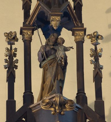 Zdjęcie nr 3: Nastawa ołtarzowa architektoniczna, jednokondygnacyjna, trójosiowa. Ołtarz kamienny, prostopadłościenny, ustawiony na dwustopniowej podstawie. Mensa kamienna, silnie wysunięta, podtrzymywana przez dwie kamienne kolumienki. Antepedium podzielone na trzy kwadratowe pola z płycinami, w środkowej wysuniętej do przodu medalion z monogramem IHS w polu. Tabernakulum w formie prostopadłościennej skrzynki, obitej fakturowaną blachą, od frontu ujęte parą kolumienek. Drzwiczki w kształcie stojącego prostokąta, dwuskrzydłowe z trybowanym przedstawieniem kielicha z unoszącą się Hostią w glorii, adorowaną przez dwa klęczące anioły. Tron do wystawiania monstrancji w formie baldachimu podtrzymywanego przez cztery kolumienki oraz z zabudowaną ścianką tylną dekorowaną rytym wzorem z czteroliści i medalionu z monogramem IHS w glorii podtrzymywanym przez parę unoszących się aniołów. Baldachim w formie dwuspadowego daszku zwieńczonego pseudowieżyczką z krzyżem; od frontu zamknięty wimpergą. Nastawa ołtarzowa ustawiona na dwustrefowym cokole z predellą dekorowaną blendami. Osie wydzielone czterema kolumnami dźwigającymi pinakle. Oś środkowa, najszersza ujęta dwiema dwustrefowymi płytkimi niszami zakończonymi trójlistnie z półpełnymi figurkami świętych: Dominika i Izydora po prawej oraz Ambrożego i Jacka po lewej; zwieńczona wimpergą, flankowaną przez dwie figurki aniołków nakryte baldachimami w formie sterczyn. W polu nisza w formie stojącego prostokąta zamkniętego łukiem trójlistnym z płaskorzeźbionym przedstawieniem Trójcy Świętej. Osie boczne z niszami w formie stojącego prostokąta zamkniętego łukiem półkolistym z figurami św. Wojciecha (po lewej) i św. Stanisława (po prawej), zamknięte dwiema wimpergami ze sterczynami oraz jednospadowym daszkiem z ażurową wieżyczką. Zwieńczenie w formie ażurowej wieżyczki z figurką św. Józefa z Dzieciątkiem, zakończonej dużą sterczyną z krzyżem dekorowaną żabkami. Struktura w kolorze naturalnego drewna, profile i ornamentyka złocone, tło pola środkowego w kolorze błękitnym, detale zielone.
