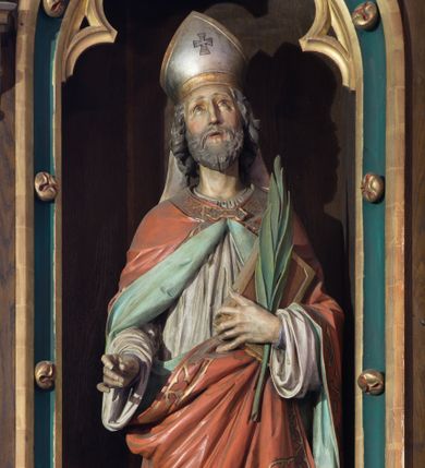 Zdjęcie nr 1: Rzeźba wolnostojąca, pełnoplastyczna ukazująca św. Wojciecha w postawie stojącej w delikatnym kontrapoście. Prawa ręka wysunięta do przodu, w której niegdyś znajdował się niezachowany atrybut świętego, w lewej trzyma księgę oraz palmę męczeństwa. Twarz podłużna, o wzroku skierowanym do góry, długim i wąskim nosie, małych ustach, okolona krótką brodą, policzki delikatnie zarumienione. Włosy siwe, falowane, zasłaniające uszy. Święty jest ubrany w fioletową albę, białą komżę i czerwoną kapę o jasnozielonej podszewce, spiętą na szyi klamrą i zdobioną na brzegach ornamentalnym pasem złożonym z trójlistnych form. Na głowie ma srebrną infułę o złoconych brzegach z równoramiennym krzyżykiem pośrodku i taśmami opadającymi na plecy. Polichromia naturalistyczna w odsłoniętych partiach ciała, atrybuty i elementy stroju złocone, palma męczeństwa w kolorze zielonym. Rzeźba ustawiona na niskim postumencie o ściętych narożach.

