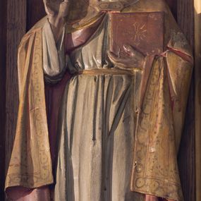 Zdjęcie nr 1: Rzeźba św. Grzegorza Wielkiego wolnostojąca, ustawiona na niskim cokole. Święty ukazany w postawie stojącej, frontalnie z prawą ręką uniesioną w geście błogosławieństwa, z księgą w lewej dłoni. Twarz szeroka o wyraźnie zaznaczonych kościach policzkowych, z długim i wąskim nosem, małymi ustami, oczach skierowanych ku górze i zmarszczonych brwiach. Spod złoconej tiary widoczne średniej długości, siwe włosy, zasłaniające uszy. Święty ubrany jest w białą albę, przewiązaną złoconym sznurem oraz złoconą kapę z czerwoną podszewką, spiętą na piersi złoconą klamrą, na stopach ma brązowe buty. Kapa dekorowana malowanym na bordowo ornamentem geometrycznym i stylizowaną wicią. Księga w czerwonej oprawie, na przodzie zdobiona malowanym na złoto greckim krzyżykiem umieszczonym w polu złoconej ramy.