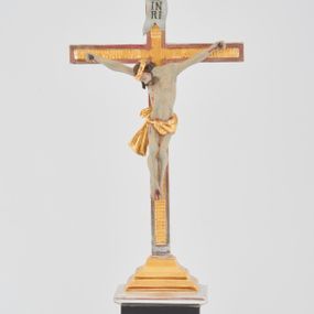 Zdjęcie nr 1: Podstawa w formie prostego prostopadłościanu na niskim cokoliku, zwieńczona gzymsem, wyżej przechodząca w zwężający się, profilowany cokół na planie prostokąta, na którym osadzony jest krucyfiks. Ramiona krzyża ujęte przy krawędzi bordową opaską, wewnątrz złocone i karbowane. Figura Chrystusa ścięta z tyłu, przybita do krzyża trzema gwoździami. Ciało w delikatnym zwisie o szeroko rozłożonych ramionach, głowa opada na prawe ramię, nogi są ugięte w kolanach, kolana przylegają do siebie, a stopy są przebite w układzie prawa na lewą. Twarz szczupła o ostrym profilu nosa, okolona krótką brodą. Włosy długie, silnie skręcone w pukle i opadające na tył głowy i prawe ramię. Ciało szczupłe o delikatnie podkreślonej muskulaturze oraz uwypuklonej formie klatki piersiowej, szczególnie linii żeber z zaznaczonymi śladami męki. Na głowie korona cierniowa. Przez biodra przewiązane jest złocone perizonium w formie krótkiej skręconej tkaniny, zawieszonej na sznurze, odsłaniającej prawe biodro, ze zwisem na prawym boku. Na zakończeniu pionowej belki titulus w formie zwoju z napisem „IN / RI”. Polichromia w odsłoniętych partiach ciała Chrystusa delikatnie sina, perizonium, krzyż i detale złocone oraz srebrzone, postument polichromowany na czarno. 
