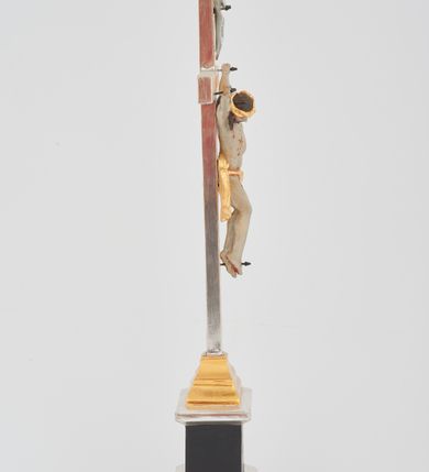 Zdjęcie nr 2: Podstawa w formie prostego prostopadłościanu na niskim cokoliku, zwieńczona gzymsem, wyżej przechodząca w zwężający się, profilowany cokół na planie prostokąta, na którym osadzony jest krucyfiks. Ramiona krzyża ujęte przy krawędzi bordową opaską, wewnątrz złocone i karbowane. Figura Chrystusa ścięta z tyłu, przybita do krzyża trzema gwoździami. Ciało w delikatnym zwisie o szeroko rozłożonych ramionach, głowa opada na prawe ramię, nogi są ugięte w kolanach, kolana przylegają do siebie, a stopy są przebite w układzie prawa na lewą. Twarz szczupła o ostrym profilu nosa, okolona krótką brodą. Włosy długie, silnie skręcone w pukle i opadające na tył głowy i prawe ramię. Ciało szczupłe o delikatnie podkreślonej muskulaturze oraz uwypuklonej formie klatki piersiowej, szczególnie linii żeber z zaznaczonymi śladami męki. Na głowie korona cierniowa. Przez biodra przewiązane jest złocone perizonium w formie krótkiej skręconej tkaniny, zawieszonej na sznurze, odsłaniającej prawe biodro, ze zwisem na prawym boku. Na zakończeniu pionowej belki titulus w formie zwoju z napisem „IN / RI”. Polichromia w odsłoniętych partiach ciała Chrystusa delikatnie sina, perizonium, krzyż i detale złocone oraz srebrzone, postument polichromowany na czarno. 
