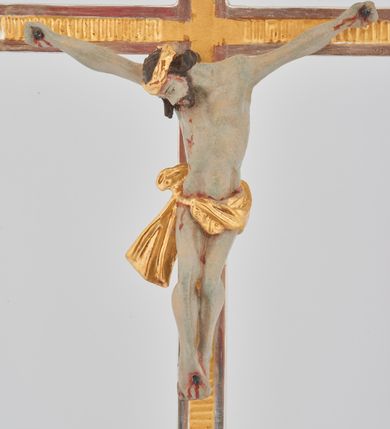 Zdjęcie nr 4: Podstawa w formie prostego prostopadłościanu na niskim cokoliku, zwieńczona gzymsem, wyżej przechodząca w zwężający się, profilowany cokół na planie prostokąta, na którym osadzony jest krucyfiks. Ramiona krzyża ujęte przy krawędzi bordową opaską, wewnątrz złocone i karbowane. Figura Chrystusa ścięta z tyłu, przybita do krzyża trzema gwoździami. Ciało w delikatnym zwisie o szeroko rozłożonych ramionach, głowa opada na prawe ramię, nogi są ugięte w kolanach, kolana przylegają do siebie, a stopy są przebite w układzie prawa na lewą. Twarz szczupła o ostrym profilu nosa, okolona krótką brodą. Włosy długie, silnie skręcone w pukle i opadające na tył głowy i prawe ramię. Ciało szczupłe o delikatnie podkreślonej muskulaturze oraz uwypuklonej formie klatki piersiowej, szczególnie linii żeber z zaznaczonymi śladami męki. Na głowie korona cierniowa. Przez biodra przewiązane jest złocone perizonium w formie krótkiej skręconej tkaniny, zawieszonej na sznurze, odsłaniającej prawe biodro, ze zwisem na prawym boku. Na zakończeniu pionowej belki titulus w formie zwoju z napisem „IN / RI”. Polichromia w odsłoniętych partiach ciała Chrystusa delikatnie sina, perizonium, krzyż i detale złocone oraz srebrzone, postument polichromowany na czarno. 

