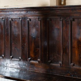 Zdjęcie nr 1: Drewniane ławki kolatorskie ustawione po obu stronach prezbiterium. Ławki ustawione na dwóch nóżkach, siedzisko proste w postaci prostej ławy. Zaplecek flankowany filarkami podtrzymującymi wyłamane, niepełne belkowanie, zamknięte gzymsem. Na osi filarków ustawione wazony. Zaplecek zdobiony pięcioma płycinami w kształcie stojących prostokątów o uszatych narożach. Ścianki boczne z przodu o wklęsło-wypukłym brzegu, sięgające do wysokości połowy zaplecka, na zakończeniu zdobione liśćmi stylizowanego akantu. Struktura pokryta bejcą.
