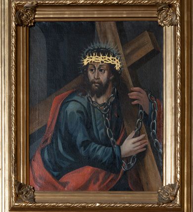 Zdjęcie nr 1: Obraz w kształcie stojącego prostokąta, ujęty profilowaną, złoconą ramą z motywem rocaille'owych kartuszy w narożach i jednego z profilowań ozdobionego motywem sznura. Chrystus ukazany jest w ujęciu półpostaciowym w trzech czwartych zwrócony w lewo z głową skierowaną w prawo. Zbawiciel oburącz podtrzymuje niesiony na lewym barku brązowy, prosty krzyż. Twarz podłużna o wyrazistych rysach i śniadej karnacji z krótkim i ciemnobrązowym zarostem, długim nosem i ciemnymi oczami. Włosy długie, ciemnobrązowe, falowane, opadające na plecy i ramiona. Na głowie ma dwie korony cierniowe, jedną czarną i drugą domalowaną poniżej, złoconą; wokół głowy promienisty nimb. Ubrany jest w ciemnoniebieską suknię i czerwony płaszcz odsłaniający część torsu i prawą rękę. Na szyi ma zawieszony gruby łańcuch, którego koniec przewieszony jest przez lewy nadgarstek; na ciele widoczne są strużki krwi i potu. Kolorystyka stonowana i ciemna. W tle widoczna murowana architektura z półkolistą arkadą. 