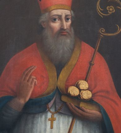 Zdjęcie nr 1: Obraz w kształcie owalu z przedstawieniem św. Mikołaja. Święty Mikołaj ukazany w półpostaci, delikatnie zwrócony w lewo, prawą dłonią czyni gest błogosławieństwa, a w lewej trzyma pastorał, zamkniętą księgę, a niej ułożone trzy złote kule. Ma twarz o rysach starszego mężczyzny, z długim nosem, dużymi oczami i wzrokiem skierowanym wprost na widza, okoloną długą i siwą brodą. Włosy średniej długości, siwe, schowane pod infułą. Święty jest ubrany w białą rokietę, fioletowy mucet i czerwoną kapę z niebieską podszewką, obwiedzioną na brzegach złotą pasmanterią. Na piersi ma zawieszony krzyż pektoralny, a na głowie czerwoną infułę. Tło obrazu jest jednolite, ciemnobrązowe. Rama drewniana, profilowana, naprzemiennie złocona i polichromowana na czarno.
