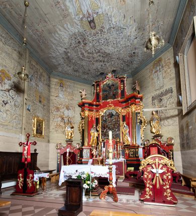Zdjęcie nr 3: Nastawa architektoniczna, dwukondygnacyjna, jednoosiowa z bramkami, na dwustrefowym cokole. Ołtarz kamienny, prostopadłościenny, w drewnianej obudowie, mensa drewniana z marmurowym portatylem. Antepedium w formie leżącego prostokąta ujętego profilowaną ramą; pole wyłożone tkaniną o kwiatowym wzorze z haftowanym medalionem w glorii z monogramem IHS; ujęty gałązkami lilii. Tabernakulum w formie drewnianej skrzynki z wypukłym frontem, obite srebrzoną blachą. Drzwiczki w kształcie stojącego prostokąta zamkniętego łukiem półkolistym, obwiedzione ramą. W polu aplikacja kielicha z hostią w glorii, ujętego kłosami zbóż; w przyłuczach ornament roślinny. Tabernakulum w architektonicznej obudowie tworzącej tron wystawienia; ujęte parą postumentów dekorowanych rocaille'owymi płycinami oraz parą filarów, przed którymi stoi para kolumn na postumentach utworzonych z ornamentalnych konsol. Podpory dźwigają belkowanie, wyłamane pośrodku, przerwane nad tabernakulum. Za tabernakulum niewielka ścianka zamknięta szczytem utworzonym z dwóch spływów wolutowych. Ze szczytu na belkowanie spływają ornamentalne woluty. Tron ujęty rocaille'owymi uszami. 
Pierwsza kondygnacja ujęta grupą zwielokrotnionych pilastrów, przed którymi stoją ustawione pod kątem cokoły z kolumnami o stylizowanych kapitelach kompozytowych, dźwigających pełne belkowanie, przerwane nad polem środkowym. Na tle pilastrów figury św. Jana Kantego po lewej stronie i św. Kazimierza po prawej. W polu środkowym obraz „Wszyscy Święci” ujęty profilowaną ramą w formie stojącego prostokąta, zamkniętego łukiem wklęsło-wypukłym z uskokami. Na zasuwie obraz przedstawiający Ukrzyżowanie Chrystusa. Druga kondygnacja w formie zbliżonej do kwadratu, flankowana przez zdwojone pilastry i spływy wolutowe, zamknięte szczytem z rocaille'owym kartuszem z napisem „OPŁUKALI / SWE SZATY / W KRWI / BARANKA / AP 7,14”. W polu obraz „Wniebowzięcie Najświętszej Marii Panny” ujęty profilowaną ramą w formie zbliżonej do kwadratu od dołu i od góry o wklęsło-wypukłym zarysie. Na zakończeniu spływów wolutowych usadzone dwie figury aniołów. Bramki w formie stojącego prostokąta ujętego parą pilastrów, dźwigających spływy wolutowe, podtrzymujące postumenty dla figur św. Stanisława po lewej stronie i św. Wojciecha po prawej. Przejścia w formie stojących prostokątów, zamkniętych stylizowanymi łukami segmentowymi nadwieszonymi. Całość dekorowana ornamentem rocaille'owym oraz różanymi zwisami w partii trzonów podpór, pierwsza kondygnacja flankowana rocaille'owymi, ażurowymi uszami. Struktura polichromowana w kolorze czerwonym, z malowanymi na czarno trzonami pilastrów i profilami, złoconymi kolumnami, profilami i ornamentyką oraz srebrzonymi detalami. Według dokumentacji konserwatorskiej na odwrociach baz kolumn znajdują się napisy „Leonora Olajassy żona organisty. 1887” oraz „Leonora Olajassy - organiścina. 1887”.