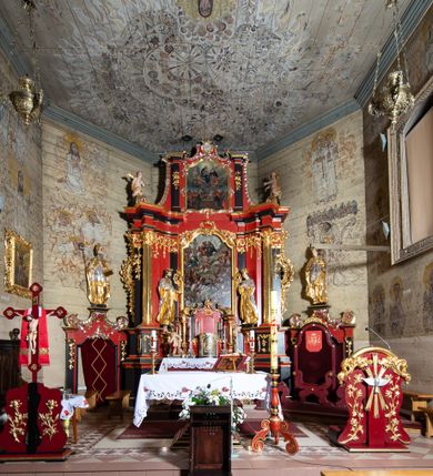 Zdjęcie nr 2: Nastawa architektoniczna, dwukondygnacyjna, jednoosiowa z bramkami, na dwustrefowym cokole. Ołtarz kamienny, prostopadłościenny, w drewnianej obudowie, mensa drewniana z marmurowym portatylem. Antepedium w formie leżącego prostokąta ujętego profilowaną ramą; pole wyłożone tkaniną o kwiatowym wzorze z haftowanym medalionem w glorii z monogramem IHS; ujęty gałązkami lilii. Tabernakulum w formie drewnianej skrzynki z wypukłym frontem, obite srebrzoną blachą. Drzwiczki w kształcie stojącego prostokąta zamkniętego łukiem półkolistym, obwiedzione ramą. W polu aplikacja kielicha z hostią w glorii, ujętego kłosami zbóż; w przyłuczach ornament roślinny. Tabernakulum w architektonicznej obudowie tworzącej tron wystawienia; ujęte parą postumentów dekorowanych rocaille'owymi płycinami oraz parą filarów, przed którymi stoi para kolumn na postumentach utworzonych z ornamentalnych konsol. Podpory dźwigają belkowanie, wyłamane pośrodku, przerwane nad tabernakulum. Za tabernakulum niewielka ścianka zamknięta szczytem utworzonym z dwóch spływów wolutowych. Ze szczytu na belkowanie spływają ornamentalne woluty. Tron ujęty rocaille'owymi uszami. 
Pierwsza kondygnacja ujęta grupą zwielokrotnionych pilastrów, przed którymi stoją ustawione pod kątem cokoły z kolumnami o stylizowanych kapitelach kompozytowych, dźwigających pełne belkowanie, przerwane nad polem środkowym. Na tle pilastrów figury św. Jana Kantego po lewej stronie i św. Kazimierza po prawej. W polu środkowym obraz „Wszyscy Święci” ujęty profilowaną ramą w formie stojącego prostokąta, zamkniętego łukiem wklęsło-wypukłym z uskokami. Na zasuwie obraz przedstawiający Ukrzyżowanie Chrystusa. Druga kondygnacja w formie zbliżonej do kwadratu, flankowana przez zdwojone pilastry i spływy wolutowe, zamknięte szczytem z rocaille'owym kartuszem z napisem „OPŁUKALI / SWE SZATY / W KRWI / BARANKA / AP 7,14”. W polu obraz „Wniebowzięcie Najświętszej Marii Panny” ujęty profilowaną ramą w formie zbliżonej do kwadratu od dołu i od góry o wklęsło-wypukłym zarysie. Na zakończeniu spływów wolutowych usadzone dwie figury aniołów. Bramki w formie stojącego prostokąta ujętego parą pilastrów, dźwigających spływy wolutowe, podtrzymujące postumenty dla figur św. Stanisława po lewej stronie i św. Wojciecha po prawej. Przejścia w formie stojących prostokątów, zamkniętych stylizowanymi łukami segmentowymi nadwieszonymi. Całość dekorowana ornamentem rocaille'owym oraz różanymi zwisami w partii trzonów podpór, pierwsza kondygnacja flankowana rocaille'owymi, ażurowymi uszami. Struktura polichromowana w kolorze czerwonym, z malowanymi na czarno trzonami pilastrów i profilami, złoconymi kolumnami, profilami i ornamentyką oraz srebrzonymi detalami. Według dokumentacji konserwatorskiej na odwrociach baz kolumn znajdują się napisy „Leonora Olajassy żona organisty. 1887” oraz „Leonora Olajassy - organiścina. 1887”.