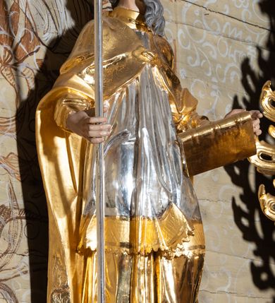 Zdjęcie nr 23: Nastawa architektoniczna, dwukondygnacyjna, jednoosiowa z bramkami, na dwustrefowym cokole. Ołtarz kamienny, prostopadłościenny, w drewnianej obudowie, mensa drewniana z marmurowym portatylem. Antepedium w formie leżącego prostokąta ujętego profilowaną ramą; pole wyłożone tkaniną o kwiatowym wzorze z haftowanym medalionem w glorii z monogramem IHS; ujęty gałązkami lilii. Tabernakulum w formie drewnianej skrzynki z wypukłym frontem, obite srebrzoną blachą. Drzwiczki w kształcie stojącego prostokąta zamkniętego łukiem półkolistym, obwiedzione ramą. W polu aplikacja kielicha z hostią w glorii, ujętego kłosami zbóż; w przyłuczach ornament roślinny. Tabernakulum w architektonicznej obudowie tworzącej tron wystawienia; ujęte parą postumentów dekorowanych rocaille'owymi płycinami oraz parą filarów, przed którymi stoi para kolumn na postumentach utworzonych z ornamentalnych konsol. Podpory dźwigają belkowanie, wyłamane pośrodku, przerwane nad tabernakulum. Za tabernakulum niewielka ścianka zamknięta szczytem utworzonym z dwóch spływów wolutowych. Ze szczytu na belkowanie spływają ornamentalne woluty. Tron ujęty rocaille'owymi uszami. 
Pierwsza kondygnacja ujęta grupą zwielokrotnionych pilastrów, przed którymi stoją ustawione pod kątem cokoły z kolumnami o stylizowanych kapitelach kompozytowych, dźwigających pełne belkowanie, przerwane nad polem środkowym. Na tle pilastrów figury św. Jana Kantego po lewej stronie i św. Kazimierza po prawej. W polu środkowym obraz „Wszyscy Święci” ujęty profilowaną ramą w formie stojącego prostokąta, zamkniętego łukiem wklęsło-wypukłym z uskokami. Na zasuwie obraz przedstawiający Ukrzyżowanie Chrystusa. Druga kondygnacja w formie zbliżonej do kwadratu, flankowana przez zdwojone pilastry i spływy wolutowe, zamknięte szczytem z rocaille'owym kartuszem z napisem „OPŁUKALI / SWE SZATY / W KRWI / BARANKA / AP 7,14”. W polu obraz „Wniebowzięcie Najświętszej Marii Panny” ujęty profilowaną ramą w formie zbliżonej do kwadratu od dołu i od góry o wklęsło-wypukłym zarysie. Na zakończeniu spływów wolutowych usadzone dwie figury aniołów. Bramki w formie stojącego prostokąta ujętego parą pilastrów, dźwigających spływy wolutowe, podtrzymujące postumenty dla figur św. Stanisława po lewej stronie i św. Wojciecha po prawej. Przejścia w formie stojących prostokątów, zamkniętych stylizowanymi łukami segmentowymi nadwieszonymi. Całość dekorowana ornamentem rocaille'owym oraz różanymi zwisami w partii trzonów podpór, pierwsza kondygnacja flankowana rocaille'owymi, ażurowymi uszami. Struktura polichromowana w kolorze czerwonym, z malowanymi na czarno trzonami pilastrów i profilami, złoconymi kolumnami, profilami i ornamentyką oraz srebrzonymi detalami. Według dokumentacji konserwatorskiej na odwrociach baz kolumn znajdują się napisy „Leonora Olajassy żona organisty. 1887” oraz „Leonora Olajassy - organiścina. 1887”.