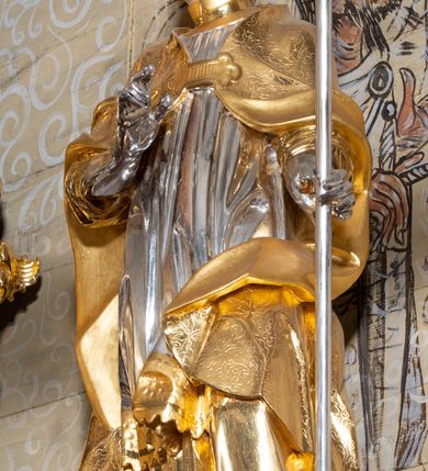 Zdjęcie nr 2: Rzeźba ścięta z tyłu, drążona, przedstawiająca św. Stanisława Biskupa. Święty ustawiony frontalnie, w delikatnym kontrapoście, w lewej ręce trzyma pastorał, prawą ugiętą w łokciu czyni gest błogosławieństwa. Twarz szeroka o silnie zaznaczonym podbródku, dużym nosie, ściągniętych brwiach, dużych oczach patrzących na wprost oraz niewielkich, rozchylonych ustach. Włosy krótkie, ciemnobrązowe i silnie skręcone po bokach głowy. Święty ubrany jest w albę, obficie drapowaną u spodu; rokietę z dekoracyjnym obszyciem u brzegu; kapę zapiętą na piersi; złocone buty, rękawice i infułę na głowie. Polichromia naturalistyczna w odsłoniętych partiach ciała, szaty i pastorał złocone i srebrzone.