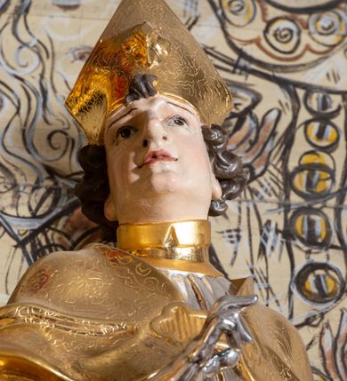 Zdjęcie nr 3: Rzeźba ścięta z tyłu, drążona, przedstawiająca św. Stanisława Biskupa. Święty ustawiony frontalnie, w delikatnym kontrapoście, w lewej ręce trzyma pastorał, prawą ugiętą w łokciu czyni gest błogosławieństwa. Twarz szeroka o silnie zaznaczonym podbródku, dużym nosie, ściągniętych brwiach, dużych oczach patrzących na wprost oraz niewielkich, rozchylonych ustach. Włosy krótkie, ciemnobrązowe i silnie skręcone po bokach głowy. Święty ubrany jest w albę, obficie drapowaną u spodu; rokietę z dekoracyjnym obszyciem u brzegu; kapę zapiętą na piersi; złocone buty, rękawice i infułę na głowie. Polichromia naturalistyczna w odsłoniętych partiach ciała, szaty i pastorał złocone i srebrzone.