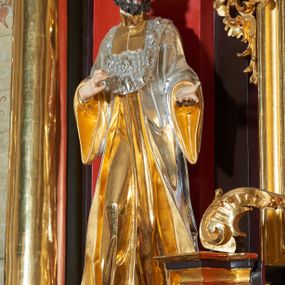 Zdjęcie nr 1: Rzeźba św. Jana Kantego, ścięta z tyłu, drążona. Święty ustawiony frontalnie w delikatnym kontrapoście z prawą nogą ugiętą w kolanie, ręce zgięte w łokciach, dłonie ułożone w teatralnych gestach. Twarz trójkątna, o uwypuklonych kościach policzkowych, dużym i bulwiastym nosie, wąskich oczach oraz niewielkich ustach; okolona krótką, gęstą i kręconą brodą. Włosy krótkie, skręcone w pukle po bokach głowy. Święty ubrany jest w długą złoconą suknię, przylegającą do ciała; togę rektorską o szerokich rękawach, rozchylającą się na boki, ze srebrzoną załogą (pelerynką) i złoconą befką; na stopach pełne buty. Polichromia naturalistyczna w odsłoniętych partiach ciała, szaty złocone i srebrzone.
