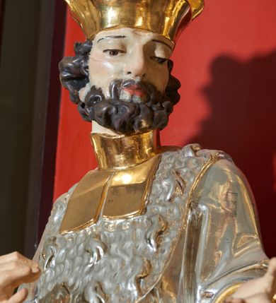 Zdjęcie nr 4: Rzeźba św. Jana Kantego, ścięta z tyłu, drążona. Święty ustawiony frontalnie w delikatnym kontrapoście z prawą nogą ugiętą w kolanie, ręce zgięte w łokciach, dłonie ułożone w teatralnych gestach. Twarz trójkątna, o uwypuklonych kościach policzkowych, dużym i bulwiastym nosie, wąskich oczach oraz niewielkich ustach; okolona krótką, gęstą i kręconą brodą. Włosy krótkie, skręcone w pukle po bokach głowy. Święty ubrany jest w długą złoconą suknię, przylegającą do ciała; togę rektorską o szerokich rękawach, rozchylającą się na boki, ze srebrzoną załogą (pelerynką) i złoconą befką; na stopach pełne buty. Polichromia naturalistyczna w odsłoniętych partiach ciała, szaty złocone i srebrzone.
