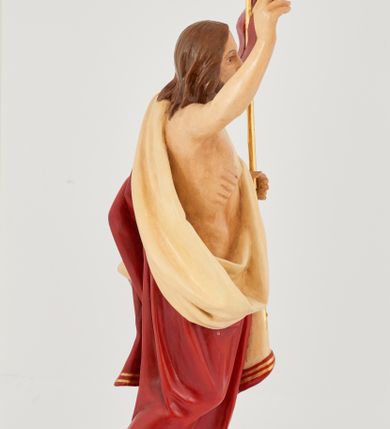 Zdjęcie nr 7: Rzeźba Chrystusa Zmartwychwstałego pełnoplastyczna, wolnostojąca. Chrystus ukazany jest w całej postaci, ustawiony frontalnie, w delikatnym kontrapoście; prawą, wysoko uniesioną ręką czyni gest błogosławieństwa, a w lewej trzyma chorągiew o długim drzewcu zakończonym krzyżem, na czerwonej tkaninie widnieje złoty krzyż. Chrystus ma podłużną twarz z długim i wąskim nosem, wzrokiem skierowanym w dal, okoloną krótką i ciemną brodą, rozdzieloną na końcu w dwa pukle oraz długie, ciemnobrązowe włosy, które opadają na plecy i ramiona. Chrystus jest ubrany w czerwony płaszcz z jasnobeżową podszewką i złoconą bordiurą, przerzucony przez lewe ramię i odsłaniający prawe ramię oraz nagi tors z drugą połą płaszcza zarzuconą na lewą rękę. Na dłoniach, stopach i boku zaznaczone są ślady męki. Polichromia ciała jest naturalistyczna. Rzeźba ustawiona jest na dwóch ukośnie ustawionych, prostopadłościennych kostkach. 