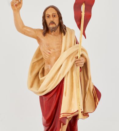Zdjęcie nr 9: Rzeźba Chrystusa Zmartwychwstałego pełnoplastyczna, wolnostojąca. Chrystus ukazany jest w całej postaci, ustawiony frontalnie, w delikatnym kontrapoście; prawą, wysoko uniesioną ręką czyni gest błogosławieństwa, a w lewej trzyma chorągiew o długim drzewcu zakończonym krzyżem, na czerwonej tkaninie widnieje złoty krzyż. Chrystus ma podłużną twarz z długim i wąskim nosem, wzrokiem skierowanym w dal, okoloną krótką i ciemną brodą, rozdzieloną na końcu w dwa pukle oraz długie, ciemnobrązowe włosy, które opadają na plecy i ramiona. Chrystus jest ubrany w czerwony płaszcz z jasnobeżową podszewką i złoconą bordiurą, przerzucony przez lewe ramię i odsłaniający prawe ramię oraz nagi tors z drugą połą płaszcza zarzuconą na lewą rękę. Na dłoniach, stopach i boku zaznaczone są ślady męki. Polichromia ciała jest naturalistyczna. Rzeźba ustawiona jest na dwóch ukośnie ustawionych, prostopadłościennych kostkach. 