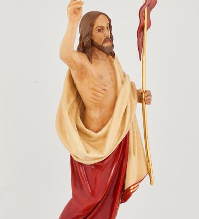 Zdjęcie nr 8: Rzeźba Chrystusa Zmartwychwstałego pełnoplastyczna, wolnostojąca. Chrystus ukazany jest w całej postaci, ustawiony frontalnie, w delikatnym kontrapoście; prawą, wysoko uniesioną ręką czyni gest błogosławieństwa, a w lewej trzyma chorągiew o długim drzewcu zakończonym krzyżem, na czerwonej tkaninie widnieje złoty krzyż. Chrystus ma podłużną twarz z długim i wąskim nosem, wzrokiem skierowanym w dal, okoloną krótką i ciemną brodą, rozdzieloną na końcu w dwa pukle oraz długie, ciemnobrązowe włosy, które opadają na plecy i ramiona. Chrystus jest ubrany w czerwony płaszcz z jasnobeżową podszewką i złoconą bordiurą, przerzucony przez lewe ramię i odsłaniający prawe ramię oraz nagi tors z drugą połą płaszcza zarzuconą na lewą rękę. Na dłoniach, stopach i boku zaznaczone są ślady męki. Polichromia ciała jest naturalistyczna. Rzeźba ustawiona jest na dwóch ukośnie ustawionych, prostopadłościennych kostkach. 