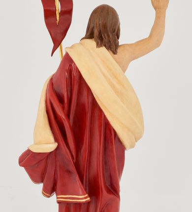 Zdjęcie nr 6: Rzeźba Chrystusa Zmartwychwstałego pełnoplastyczna, wolnostojąca. Chrystus ukazany jest w całej postaci, ustawiony frontalnie, w delikatnym kontrapoście; prawą, wysoko uniesioną ręką czyni gest błogosławieństwa, a w lewej trzyma chorągiew o długim drzewcu zakończonym krzyżem, na czerwonej tkaninie widnieje złoty krzyż. Chrystus ma podłużną twarz z długim i wąskim nosem, wzrokiem skierowanym w dal, okoloną krótką i ciemną brodą, rozdzieloną na końcu w dwa pukle oraz długie, ciemnobrązowe włosy, które opadają na plecy i ramiona. Chrystus jest ubrany w czerwony płaszcz z jasnobeżową podszewką i złoconą bordiurą, przerzucony przez lewe ramię i odsłaniający prawe ramię oraz nagi tors z drugą połą płaszcza zarzuconą na lewą rękę. Na dłoniach, stopach i boku zaznaczone są ślady męki. Polichromia ciała jest naturalistyczna. Rzeźba ustawiona jest na dwóch ukośnie ustawionych, prostopadłościennych kostkach. 