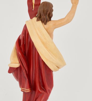 Zdjęcie nr 5: Rzeźba Chrystusa Zmartwychwstałego pełnoplastyczna, wolnostojąca. Chrystus ukazany jest w całej postaci, ustawiony frontalnie, w delikatnym kontrapoście; prawą, wysoko uniesioną ręką czyni gest błogosławieństwa, a w lewej trzyma chorągiew o długim drzewcu zakończonym krzyżem, na czerwonej tkaninie widnieje złoty krzyż. Chrystus ma podłużną twarz z długim i wąskim nosem, wzrokiem skierowanym w dal, okoloną krótką i ciemną brodą, rozdzieloną na końcu w dwa pukle oraz długie, ciemnobrązowe włosy, które opadają na plecy i ramiona. Chrystus jest ubrany w czerwony płaszcz z jasnobeżową podszewką i złoconą bordiurą, przerzucony przez lewe ramię i odsłaniający prawe ramię oraz nagi tors z drugą połą płaszcza zarzuconą na lewą rękę. Na dłoniach, stopach i boku zaznaczone są ślady męki. Polichromia ciała jest naturalistyczna. Rzeźba ustawiona jest na dwóch ukośnie ustawionych, prostopadłościennych kostkach. 