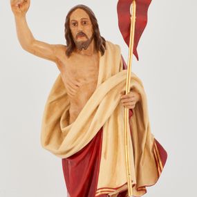 Zdjęcie nr 1: Rzeźba Chrystusa Zmartwychwstałego pełnoplastyczna, wolnostojąca. Chrystus ukazany jest w całej postaci, ustawiony frontalnie, w delikatnym kontrapoście; prawą, wysoko uniesioną ręką czyni gest błogosławieństwa, a w lewej trzyma chorągiew o długim drzewcu zakończonym krzyżem, na czerwonej tkaninie widnieje złoty krzyż. Chrystus ma podłużną twarz z długim i wąskim nosem, wzrokiem skierowanym w dal, okoloną krótką i ciemną brodą, rozdzieloną na końcu w dwa pukle oraz długie, ciemnobrązowe włosy, które opadają na plecy i ramiona. Chrystus jest ubrany w czerwony płaszcz z jasnobeżową podszewką i złoconą bordiurą, przerzucony przez lewe ramię i odsłaniający prawe ramię oraz nagi tors z drugą połą płaszcza zarzuconą na lewą rękę. Na dłoniach, stopach i boku zaznaczone są ślady męki. Polichromia ciała jest naturalistyczna. Rzeźba ustawiona jest na dwóch ukośnie ustawionych, prostopadłościennych kostkach. 