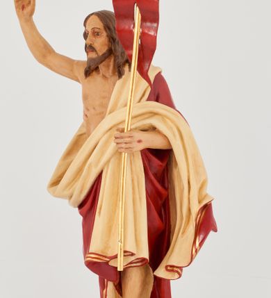 Zdjęcie nr 2: Rzeźba Chrystusa Zmartwychwstałego pełnoplastyczna, wolnostojąca. Chrystus ukazany jest w całej postaci, ustawiony frontalnie, w delikatnym kontrapoście; prawą, wysoko uniesioną ręką czyni gest błogosławieństwa, a w lewej trzyma chorągiew o długim drzewcu zakończonym krzyżem, na czerwonej tkaninie widnieje złoty krzyż. Chrystus ma podłużną twarz z długim i wąskim nosem, wzrokiem skierowanym w dal, okoloną krótką i ciemną brodą, rozdzieloną na końcu w dwa pukle oraz długie, ciemnobrązowe włosy, które opadają na plecy i ramiona. Chrystus jest ubrany w czerwony płaszcz z jasnobeżową podszewką i złoconą bordiurą, przerzucony przez lewe ramię i odsłaniający prawe ramię oraz nagi tors z drugą połą płaszcza zarzuconą na lewą rękę. Na dłoniach, stopach i boku zaznaczone są ślady męki. Polichromia ciała jest naturalistyczna. Rzeźba ustawiona jest na dwóch ukośnie ustawionych, prostopadłościennych kostkach. 