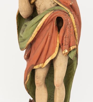 Zdjęcie nr 3: Rzeźba Chrystusa Zmartwychwstałego pełnoplastyczna, wolnostojąca, ustawiona na niskim, półkolistym cokole. Chrystus ukazany w całej postaci, ustawiony frontalnie, prawą ręką czyni gest błogosławieństwa, lewa niezachowana. Twarz podłużna, z długim nosem i małymi oczami, wysokim czołem, okolona krótką i brązową brodą, rozdzieloną na końcu w dwa małe pukle. Włosy długie, brązowe opadające na ramiona i plecy równolegle ułożonymi lokami skręconymi na końcu. Chrystus ubrany jest w czerwony płaszcz z zieloną podszewką, spięty na dekolcie złotą broszką, odsłaniający klatkę piersiową i nogi, otaczający figurę, z prawą połą przerzuconą przez lewe przedramię. Na dłoniach, stopach i boku ma delikatnie zaznaczone ślady męki. Polichromia ciała jest naturalistyczna, lamówka płaszcza złocona. 
