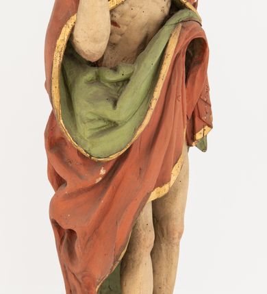 Zdjęcie nr 2: Rzeźba Chrystusa Zmartwychwstałego pełnoplastyczna, wolnostojąca, ustawiona na niskim, półkolistym cokole. Chrystus ukazany w całej postaci, ustawiony frontalnie, prawą ręką czyni gest błogosławieństwa, lewa niezachowana. Twarz podłużna, z długim nosem i małymi oczami, wysokim czołem, okolona krótką i brązową brodą, rozdzieloną na końcu w dwa małe pukle. Włosy długie, brązowe opadające na ramiona i plecy równolegle ułożonymi lokami skręconymi na końcu. Chrystus ubrany jest w czerwony płaszcz z zieloną podszewką, spięty na dekolcie złotą broszką, odsłaniający klatkę piersiową i nogi, otaczający figurę, z prawą połą przerzuconą przez lewe przedramię. Na dłoniach, stopach i boku ma delikatnie zaznaczone ślady męki. Polichromia ciała jest naturalistyczna, lamówka płaszcza złocona. 
