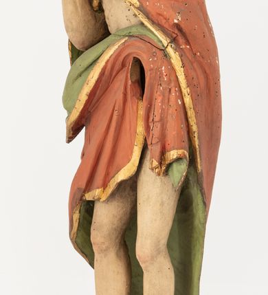 Zdjęcie nr 5: Rzeźba Chrystusa Zmartwychwstałego pełnoplastyczna, wolnostojąca, ustawiona na niskim, półkolistym cokole. Chrystus ukazany w całej postaci, ustawiony frontalnie, prawą ręką czyni gest błogosławieństwa, lewa niezachowana. Twarz podłużna, z długim nosem i małymi oczami, wysokim czołem, okolona krótką i brązową brodą, rozdzieloną na końcu w dwa małe pukle. Włosy długie, brązowe opadające na ramiona i plecy równolegle ułożonymi lokami skręconymi na końcu. Chrystus ubrany jest w czerwony płaszcz z zieloną podszewką, spięty na dekolcie złotą broszką, odsłaniający klatkę piersiową i nogi, otaczający figurę, z prawą połą przerzuconą przez lewe przedramię. Na dłoniach, stopach i boku ma delikatnie zaznaczone ślady męki. Polichromia ciała jest naturalistyczna, lamówka płaszcza złocona. 
