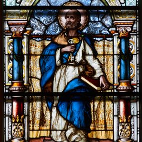 Zdjęcie nr 1: Witraż w kształcie stojącego prostokąta, zamkniętego łukiem odcinkowym. W centrum kompozycji ukazany jest św. Piotr wewnątrz dekoracyjnej aediculi. Święty przedstawiony jest frontalnie, w lewej dłoni trzyma opartą o biodro księgę, a w prawej dwa klucze, przyciśnięte do piersi, głowa uniesiona lekko do góry. Twarz szeroka z wysokim czołem z zaznaczoną łysiną na głowie, okolona bujną, krótką brodą. Święty ubrany jest w białą suknię, przewiązaną w pasie; niebieski płaszcz ze złotą podszewką, spięty na lewym ramieniu zieloną fibulą oraz sandały na stopach; wokół głowy ma kolisty nimb, wypełniony świetlistymi promieniami i złotymi zdobieniami. Aedicula wsparta jest na parach kolumn oraz stojących za nimi filarów, ustawionych na dwustopniowych cokołach. Podpory podtrzymują zwieńczenie z łukiem odcinkowym z przodu. W tle na prostym drążku, zawieszona jest drapowana, złota kotara ze złotymi frędzlami; podłoga ułożona z brązowym płytek. Cokoły kolumn dekorowane są płycinami, wypełnionymi rozetami i wolutami. Kolumny w połowie przedzielone są opaską, u dołu zdobione stylizowanymi liśćmi akantu, a u góry zielonym festonem. W dolnej części kolumny są koloru czerwonego, w górnej niebieskiego; kapitele kompozytowe. Trzony filarów zdobione prostokątnymi płycinami, wypełnionymi roślinną dekoracją. Łuk zdobiony jest złoconą wicią roślinną i astragalem, w kluczu znajduje się uskrzydlona główka aniołka z czerwonymi skrzydłami. Zwieńczenie dwustopniowe, bogato dekorowane wolutkami i liśćmi akantu, na szczycie przerwany przyczółek, a po środku wazon. W dolnej partii witrażu, pomiędzy cokołami aediculi ozdobny kartusz zdobiony stylizowanym ornamentem okuciowym z prostokątną płyciną w polu z napisem: „S[ANC]T[US] PETRUS” oraz sygnatura artysty Georga Boosa z Monachium.


