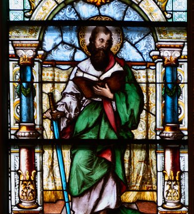 Zdjęcie nr 2: Witraż w kształcie stojącego prostokąta, zamkniętego łukiem odcinkowym. W centrum kompozycji ukazany jest św. Paweł wewnątrz dekoracyjnej aediculi. Święty przedstawiony jest frontalnie, w lewej dłoni trzyma otwartą księgę, a w prawej miecz skierowany ostrzem w dół, głowa skłoniona jest lekko w dół, w stronę księgi. Twarz podłużna w wysokim czołem z zakolami, okolona bujną, długą i ciemnobrązową brodą. Święty ubrany jest w jasnoróżową suknię, zielony płaszcz z czerwoną podszewką, przewieszony przez lewe ramię oraz sandały na stopach; wokół głowy ma kolisty nimb, wypełniony świetlistymi promieniami i złotymi zdobieniami. Aedicula wsparta jest na parach kolumn oraz stojących za nimi filarów, ustawionych na dwustopniowych cokołach. Podpory podtrzymują zwieńczenie z łukiem odcinkowym z przodu. W tle na prostym drążku, zawieszona jest drapowana, złota kotara ze złotymi frędzlami; podłoga ułożona z brązowym płytek. Cokoły kolumn dekorowane są płycinami, wypełnionymi rozetami. Kolumny w połowie przedzielone są opaską, u dołu zdobione stylizowanymi liśćmi akantu, a u góry zielonym festonem. W dolnej części kolumny są koloru czerwonego, w górnej niebieskiego; kapitele kompozytowe. Trzony filarów zdobione prostokątnymi płycinami, wypełnionymi roślinną dekoracją. Łuk zdobiony jest złoconą wicią roślinną i astragalem, w kluczu znajduje się uskrzydlona główka aniołka z czerwonymi skrzydłami. Zwieńczenie dwustopniowe, bogato dekorowane wolutkami i liśćmi akantu, na szczycie przerwany przyczółek, a po środku wazon. W dolnej partii witrażu, pomiędzy cokołami aediculi ozdobny kartusz zdobiony stylizowanym ornamentem okuciowym z prostokątną płyciną w polu z napisem: „S[ANC]T[US] PAULUS” oraz sygnatura artysty Georga Boosa z Monachium.