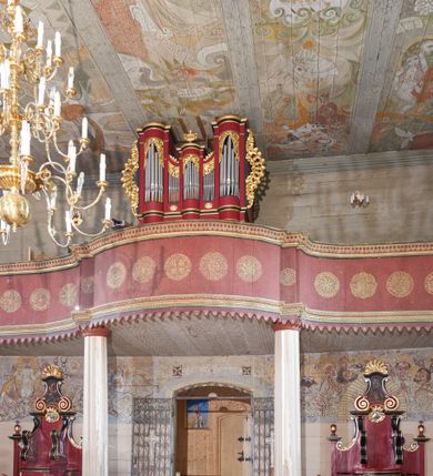 Zdjęcie nr 1: Prospekt organowy architektoniczny, jednokondygnacyjny, pięcioosiowy na cokole. Osie skrajne i oś środkowa są wypukłe, wydzielone ryzalitami z prześwitami wypełnionymi piszczałkami; zwieńczone profilowanym gzymsem. Analogicznie ukształtowany cokolik ujmuje strukturę od dołu. Osie zewnętrzne sięgają stropu, środkowa niższa połączona jest z nimi płaskimi ściankami z prześwitami na piszczałki. Organy ujęte są ażurowymi uszami utworzonymi z wici roślinnej. Na osi środkowej ustawiony jest klasycystyczny wazon. Prześwity w górnej partii każdej osi wypełniają stylizowane liście akantu. Struktura polichromowana w kolorze czerwonym; profilowania złocone i polichromowane na czarno, ornamentyka złocona.