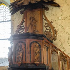 Zdjęcie nr 1: Ambona przyścienna, koszowa, z dostępem od zachodu w postaci jednobiegowych schodów z ażurową dekorowaną stylizowanymi blendami balustradą. Oparty na słupie w formie pnia drzewa, które korzeniami wchodzi w trójstopniową podstawę kosz na planie ściętego ośmioboku. Pola ścianek w formie płycin zamkniętych łukiem półkolistym z motywem fryzu arkadkowego. Przed każdą z płycin, ustawiona na konsolce całopostaciowa figurka jednego z czterech ewangelistów trzymających w dłoniach atrybuty (św. Mateusz z księgą i piórem, św. Łukasz ze zwojem i stylusem, św. Jan z kielichem z wężem, św. Marek z księgą). Podstawę kosza obiega gzyms, podwieszenie ujmują konary w promienistym układzie, pomiędzy którymi są symbole ewangelistów: anioł, wół, orzeł i lew. Parapet w formie wklęsło-wypukłego gzymsu. Zaplecek w kształcie stojącego prostokąta, ujętego ramą oraz parą ażurowych wolut; w polu arkada z płaskorzeźbionym przedstawieniem Chrystusa niosącego krzyż, w szczycie napis IHS ujęty wiązkami promienistej glorii. Baldachim utworzony z palmowych liści. Na podniebiu gołębicą Ducha Świętego w glorii promienistej.