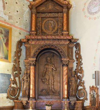 Zdjęcie nr 1: Ołtarz architektoniczny, jednokondygnacyjny, jednoosiowy ze zwieńczeniem. Ołtarz prostopadłościenny z drewnianą mensą, po bokach ujęty uskokowo. Retabulum osadzone na niewysokim, podwójnie zryzalitowanym po bokach cokole, skrajne partie ustawione ukośnie. Część środkowa w formie półkoliście zamkniętej arkady wspartej na parze kolumn i ujętej parą pilastrów. Całość wieńczy wyłamujące się w części środkowej belkowanie. Zwieńczenie ujmuje para kolumn osadzonych na niewielkich cokołach i wspierających gzyms w kształcie trójkątnego przyczółka. Pola uskokowych boków ołtarza zdobią motywy S-kształtnych, ulistnionych wolut, pole antepedium wypełnia fryz arkadkowy. Partie cokołu retabulum zdobią motywy rozet. W kapitelach kolumn jest dekoracja w formie uskrzydlonych główek anielskich. Łuk arkady zdobi ażurowy fryz arkadkowy, natomiast górne pola tej części retabulum motywy czwórliści i S-kształtnych, ulistnionych wolut. Zarówno środkową część retabulum, jak i zwieńczenie ujmują po bokach pary ażurowych uszaków w formie wici  roślinnej. W polu przyczółka jest płaskorzeźbiona promienista gloria z monogramem imienia Jezus pośrodku. Szczyt zwieńczenia w formie krzyża, ujęty po bokach parą wazonów. Pole arkady części środkowej retabulum wypełnia płaskorzeźbiona sylwetka św. Floriana, natomiast po bokach, na tle pilastrów została ustawiona para figur św. Barbary po lewej stronie i św. Szymona po prawej. Pole zwieńczenia w kształcie zbliżonym do kwadratu, ujęte szerokim obramieniem zdobionym ażurowym ornamentem w formie S-kształtnych, ulistnionych wolut. W środku tondo z płaskorzeźbionym wizerunkiem św. Marii Magdaleny. 
Struktura retabulum utrzymana w kolorze drewna, trzony kolumn i część detali architektonicznych marmoryzowane.         
