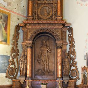 Zdjęcie nr 1: Ołtarz architektoniczny, jednokondygnacyjny, jednoosiowy ze zwieńczeniem. Ołtarz prostopadłościenny z drewnianą mensą, po bokach ujęty uskokowo. Retabulum osadzone na niewysokim, podwójnie zryzalitowanym po bokach cokole, skrajne partie ustawione ukośnie. Część środkowa w formie półkoliście zamkniętej arkady wspartej na parze kolumn i ujętej parą pilastrów. Całość wieńczy wyłamujące się w części środkowej belkowanie. Zwieńczenie ujmuje para kolumn osadzonych na niewielkich cokołach i wspierających gzyms w kształcie trójkątnego przyczółka. Pola uskokowych boków ołtarza zdobią motywy S-kształtnych, ulistnionych wolut, pole antepedium wypełnia fryz arkadkowy. Partie cokołu retabulum zdobią motywy rozet. W kapitelach kolumn jest dekoracja w formie uskrzydlonych główek anielskich. Łuk arkady zdobi ażurowy fryz arkadkowy, natomiast górne pola tej części retabulum motywy czwórliści i S-kształtnych, ulistnionych wolut. Zarówno środkową część retabulum, jak i zwieńczenie ujmują po bokach pary ażurowych uszaków w formie wici  roślinnej. W polu przyczółka jest płaskorzeźbiona promienista gloria z monogramem imienia Jezus pośrodku. Szczyt zwieńczenia w formie krzyża, ujęty po bokach parą wazonów. Pole arkady części środkowej retabulum wypełnia płaskorzeźbiona sylwetka św. Floriana, natomiast po bokach, na tle pilastrów została ustawiona para figur św. Barbary po lewej stronie i św. Szymona po prawej. Pole zwieńczenia w kształcie zbliżonym do kwadratu, ujęte szerokim obramieniem zdobionym ażurowym ornamentem w formie S-kształtnych, ulistnionych wolut. W środku tondo z płaskorzeźbionym wizerunkiem św. Marii Magdaleny. 
Struktura retabulum utrzymana w kolorze drewna, trzony kolumn i część detali architektonicznych marmoryzowane.         
