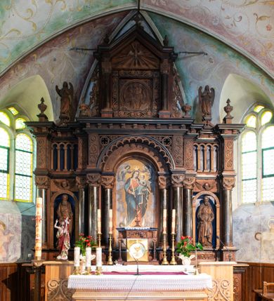 Zdjęcie nr 1: Ołtarz architektoniczny, jednokondygnacyjny, trójosiowy, ze zwieńczeniem. Ołtarz prostopadłościenny, kamienny, ustawiony na podstawie, w drewnianej obudowie. Mensa drewniana z marmurowym portatylem. Tabernakulum w formie prostopadłościennej metalowej skrzynki w drewnianej obudowie. Metalowe drzwiczki zdobi motyw kielicha eucharystycznego. Tabernakulum ujęte jest po bokach parą wolnostojących kolumienek wspierających wysunięte ponad nimi, wieńczące je belkowanie z wysokim fryzem. W partii belkowania nad drzwiczkami arkada dekorowana koronką i maswerkowymi rozetami w przyłuczach. Na belkowaniu tron wystawienia, na którym ustawiony krucyfiks. Osadzona na cokole nastawa ołtarza ma formę trójprzelotowego łuku triumfalnego. Część środkowa w kształcie półkolistej arkady wspartej na dwóch parach kolumn, z których wewnętrzne są cofnięte względem zewnętrznych. Arkady artykułujące osie boczne są mniejsze, ujmuje je po jednej parze kolumn wspierających zryzalitowane cokoły flankujące pola wypełnione fryzem arkadkowym. Zwieńczenie ołtarza ujmuje para kolumn wspierających gzyms w formie trójkątnego przyczółka. Pola cokołów retabulum zdobi stylizowana ornamentyka roślinna, kapitele kolumn oraz zwieńczenia arkad osi bocznych motywy uskrzydlonych główek anielskich. Krawędź łuku arkady części środkowej obiega fryz arkadkowy. W przyłuczach arkady ażurowe maswerki. Gzyms wieńczący kondygnację retabulum ujmuje motyw konsolek w formie liści akantu. Zwieńczenie flankowane parą ażurowych uszaków w postaci ornamentu roślinnego, parą figur aniołów oraz dwiema parami wazonów. Pole przyczółka wypełnia płaskorzeźbione przedstawienie gołębicy Ducha Świętego na tle promienistej glorii. Po jego bokach znajduje się para wazonów, szczyt jest w formie krzyża. Zwieńczenie flankują dwie figury aniołów ujęte po bokach dwoma parami wazonów.  
Pole części środkowej w kształcie stojącego prostokąta zamkniętego półkoliście z obrazem Madonny z Dzieciątkiem. W niszach osi bocznych są figury św. Piotra po prawej stronie i św. Pawła po lewej. Kształt pola zwieńczenia jest zbliżony do kwadratu ujętego szerokim obramieniem zdobionym parami S-kształtnych wolut. W środku znajduje się tondo z płaskorzeźbionym przedstawieniem anioła trzymającego kwiat lilii. 

Struktura retabulum utrzymana w kolorze drewna, trzony kolumn i część detali architektonicznych marmoryzowane, tła osi bocznych polichromowane w kolorze ciemnoniebieskim.    

