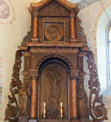 Zdjęcie nr 1: Ołtarz architektoniczny, jednokondygnacyjny, jednoosiowy ze zwieńczeniem. Ołtarz prostopadłościenny z drewnianą mensą, po bokach ujęty uskokowo. Retabulum osadzone na niewysokim, podwójnie zryzalitowanym po bokach cokole, skrajne partie ustawione ukośnie. Część środkowa w formie półkoliście zamkniętej arkady wspartej na parze kolumn i ujętej parą pilastrów. Całość wieńczy wyłamujące się w części środkowej belkowanie. Zwieńczenie ujmuje para kolumn osadzonych na niewielkich cokołach i wspierających gzyms w kształcie trójkątnego przyczółka. Pola uskokowych boków ołtarza zdobią motywy S-kształtnych, ulistnionych wolut, pole antepedium wypełnia fryz arkadkowy. Partie cokołu retabulum zdobią motywy rozet. W kapitelach kolumn jest dekoracja w formie uskrzydlonych główek anielskich. Łuk arkady zdobi ażurowy fryz arkadkowy, natomiast górne pola tej części retabulum motywy czwórliści i S-kształtnych, ulistnionych wolut. Zarówno środkową część retabulum, jak i zwieńczenie ujmują po bokach pary ażurowych uszaków w formie wici roślinnej. W polu przyczółka jest płaskorzeźbiona promienista gloria z monogramem maryjnym pośrodku. Szczyt zwieńczenia w formie krzyża. Pole arkady części środkowej retabulum wypełnia płaskorzeźbiona sylwetka św. Michała Archanioła, natomiast po bokach, na tle pilastrów została ustawiona para figur św. Katarzyny Aleksandryjskiej po prawej stronie i św. Andrzeja po lewej. Pole zwieńczenia w kształcie zbliżonym do kwadratu, ujęte szerokim obramieniem zdobionym ażurowym ornamentem w formie S-kształtnych, ulistnionych wolut. W środku jest tondo z płaskorzeźbionym wizerunkiem św. Jana Chrzciciela. 
Struktura retabulum utrzymana w kolorze drewna, trzony kolumn i część detali architektonicznych marmoryzowane.         
