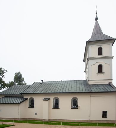 Zdjęcie nr 5: Kościół orientowany, murowany, jednonawowy, z trójbocznie zamkniętym prezbiterium z zakrystią od północy i kruchtą przylegającą do nawy od południa. Prezbiterium jest niższe i węższe od nawy, obie części mają gładkie ściany przeprute jedynie oknami w kształcie stojącego prostokąta zamkniętego łukiem półkolistym – cztery w prezbiterium, sześć w nawie. Sklepienia obu części zwierciadlane. Od południa chór o prostej balustradzie, wsparty na dwóch kolumnach. Ściany pokrywa polichromia ze scenami i cytatami z Pisma Świętego, postaciami świętych oraz żyjących, a także o motywach dekoracyjnych – roślinnych. Do około jednej czwartej wysokości ścian okładzina.  Zachodnią elewację frontową kościoła tworzy trójosiowa, wieżowa fasada. Oś kompozycji stanowi wysunięta ryzalitowo czterokondygnacyjna wieża. Ściana czołowa wieży dekorowana w pierwszej i drugiej kondygnacji boniowaniem i oknami w kształcie leżącego prostokąta osłoniętymi ozdobną kratą, z portalem o wykroju prostokątnym, ponad którym napis „DEO SOLI GLORIA”. W drugiej i trzeciej kondygnacji okna o wykroju stojącego prostokąta zamkniętego łukiem pełnym. Niżej w płycinie zwieńczonej łukiem nadwieszonym, wyżej w prostokątnej. Kondygnacje rozdzielone za pomocą masywnych gzymsów. Całość zwieńczona dachem namiotowym z kulą i krzyżem. Osie boczne cofnięte w stosunku do wysuniętej wieży i zrytmizowane podziałem ramowym, wypełnione wklęsłą płyciną w formie wydłużonego, stojącego prostokąta. Nad gzymsem fragment przyczółka przysłonięty wieżą. Elewacje boczne i tylna ukształtowane jednorodnie, gładkie, przeprute jedynie oknami. Wszystkie dachy blaszane – nad nawą i kruchtą dwuspadowy, nad zakrystią pulpitowy, nad prezbiterium zamknięty wielobocznie. 
Wartymi uwagi elementami wyposażenia kościoła jest siedemnastowieczny ołtarz boczny prawy z późniejszymi o wiek wizerunkami św. Katarzyny i św. Wawrzyńca, bogato rzeźbiona ława kolatorska i siedemnastowieczna chrzcielnica. 