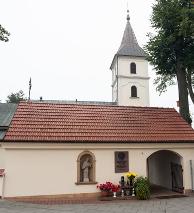 Zdjęcie nr 16: Kościół orientowany, murowany, jednonawowy, z trójbocznie zamkniętym prezbiterium z zakrystią od północy i kruchtą przylegającą do nawy od południa. Prezbiterium jest niższe i węższe od nawy, obie części mają gładkie ściany przeprute jedynie oknami w kształcie stojącego prostokąta zamkniętego łukiem półkolistym – cztery w prezbiterium, sześć w nawie. Sklepienia obu części zwierciadlane. Od południa chór o prostej balustradzie, wsparty na dwóch kolumnach. Ściany pokrywa polichromia ze scenami i cytatami z Pisma Świętego, postaciami świętych oraz żyjących, a także o motywach dekoracyjnych – roślinnych. Do około jednej czwartej wysokości ścian okładzina.  Zachodnią elewację frontową kościoła tworzy trójosiowa, wieżowa fasada. Oś kompozycji stanowi wysunięta ryzalitowo czterokondygnacyjna wieża. Ściana czołowa wieży dekorowana w pierwszej i drugiej kondygnacji boniowaniem i oknami w kształcie leżącego prostokąta osłoniętymi ozdobną kratą, z portalem o wykroju prostokątnym, ponad którym napis „DEO SOLI GLORIA”. W drugiej i trzeciej kondygnacji okna o wykroju stojącego prostokąta zamkniętego łukiem pełnym. Niżej w płycinie zwieńczonej łukiem nadwieszonym, wyżej w prostokątnej. Kondygnacje rozdzielone za pomocą masywnych gzymsów. Całość zwieńczona dachem namiotowym z kulą i krzyżem. Osie boczne cofnięte w stosunku do wysuniętej wieży i zrytmizowane podziałem ramowym, wypełnione wklęsłą płyciną w formie wydłużonego, stojącego prostokąta. Nad gzymsem fragment przyczółka przysłonięty wieżą. Elewacje boczne i tylna ukształtowane jednorodnie, gładkie, przeprute jedynie oknami. Wszystkie dachy blaszane – nad nawą i kruchtą dwuspadowy, nad zakrystią pulpitowy, nad prezbiterium zamknięty wielobocznie. 
Wartymi uwagi elementami wyposażenia kościoła jest siedemnastowieczny ołtarz boczny prawy z późniejszymi o wiek wizerunkami św. Katarzyny i św. Wawrzyńca, bogato rzeźbiona ława kolatorska i siedemnastowieczna chrzcielnica. 