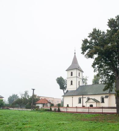 Zdjęcie nr 14: Kościół orientowany, murowany, jednonawowy, z trójbocznie zamkniętym prezbiterium z zakrystią od północy i kruchtą przylegającą do nawy od południa. Prezbiterium jest niższe i węższe od nawy, obie części mają gładkie ściany przeprute jedynie oknami w kształcie stojącego prostokąta zamkniętego łukiem półkolistym – cztery w prezbiterium, sześć w nawie. Sklepienia obu części zwierciadlane. Od południa chór o prostej balustradzie, wsparty na dwóch kolumnach. Ściany pokrywa polichromia ze scenami i cytatami z Pisma Świętego, postaciami świętych oraz żyjących, a także o motywach dekoracyjnych – roślinnych. Do około jednej czwartej wysokości ścian okładzina.  Zachodnią elewację frontową kościoła tworzy trójosiowa, wieżowa fasada. Oś kompozycji stanowi wysunięta ryzalitowo czterokondygnacyjna wieża. Ściana czołowa wieży dekorowana w pierwszej i drugiej kondygnacji boniowaniem i oknami w kształcie leżącego prostokąta osłoniętymi ozdobną kratą, z portalem o wykroju prostokątnym, ponad którym napis „DEO SOLI GLORIA”. W drugiej i trzeciej kondygnacji okna o wykroju stojącego prostokąta zamkniętego łukiem pełnym. Niżej w płycinie zwieńczonej łukiem nadwieszonym, wyżej w prostokątnej. Kondygnacje rozdzielone za pomocą masywnych gzymsów. Całość zwieńczona dachem namiotowym z kulą i krzyżem. Osie boczne cofnięte w stosunku do wysuniętej wieży i zrytmizowane podziałem ramowym, wypełnione wklęsłą płyciną w formie wydłużonego, stojącego prostokąta. Nad gzymsem fragment przyczółka przysłonięty wieżą. Elewacje boczne i tylna ukształtowane jednorodnie, gładkie, przeprute jedynie oknami. Wszystkie dachy blaszane – nad nawą i kruchtą dwuspadowy, nad zakrystią pulpitowy, nad prezbiterium zamknięty wielobocznie. 
Wartymi uwagi elementami wyposażenia kościoła jest siedemnastowieczny ołtarz boczny prawy z późniejszymi o wiek wizerunkami św. Katarzyny i św. Wawrzyńca, bogato rzeźbiona ława kolatorska i siedemnastowieczna chrzcielnica. 