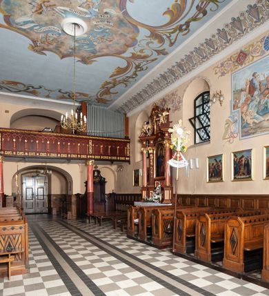 Zdjęcie nr 20: Kościół orientowany, murowany, jednonawowy, z trójbocznie zamkniętym prezbiterium z zakrystią od północy i kruchtą przylegającą do nawy od południa. Prezbiterium jest niższe i węższe od nawy, obie części mają gładkie ściany przeprute jedynie oknami w kształcie stojącego prostokąta zamkniętego łukiem półkolistym – cztery w prezbiterium, sześć w nawie. Sklepienia obu części zwierciadlane. Od południa chór o prostej balustradzie, wsparty na dwóch kolumnach. Ściany pokrywa polichromia ze scenami i cytatami z Pisma Świętego, postaciami świętych oraz żyjących, a także o motywach dekoracyjnych – roślinnych. Do około jednej czwartej wysokości ścian okładzina.  Zachodnią elewację frontową kościoła tworzy trójosiowa, wieżowa fasada. Oś kompozycji stanowi wysunięta ryzalitowo czterokondygnacyjna wieża. Ściana czołowa wieży dekorowana w pierwszej i drugiej kondygnacji boniowaniem i oknami w kształcie leżącego prostokąta osłoniętymi ozdobną kratą, z portalem o wykroju prostokątnym, ponad którym napis „DEO SOLI GLORIA”. W drugiej i trzeciej kondygnacji okna o wykroju stojącego prostokąta zamkniętego łukiem pełnym. Niżej w płycinie zwieńczonej łukiem nadwieszonym, wyżej w prostokątnej. Kondygnacje rozdzielone za pomocą masywnych gzymsów. Całość zwieńczona dachem namiotowym z kulą i krzyżem. Osie boczne cofnięte w stosunku do wysuniętej wieży i zrytmizowane podziałem ramowym, wypełnione wklęsłą płyciną w formie wydłużonego, stojącego prostokąta. Nad gzymsem fragment przyczółka przysłonięty wieżą. Elewacje boczne i tylna ukształtowane jednorodnie, gładkie, przeprute jedynie oknami. Wszystkie dachy blaszane – nad nawą i kruchtą dwuspadowy, nad zakrystią pulpitowy, nad prezbiterium zamknięty wielobocznie. 
Wartymi uwagi elementami wyposażenia kościoła jest siedemnastowieczny ołtarz boczny prawy z późniejszymi o wiek wizerunkami św. Katarzyny i św. Wawrzyńca, bogato rzeźbiona ława kolatorska i siedemnastowieczna chrzcielnica. 