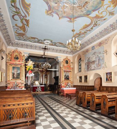 Zdjęcie nr 18: Kościół orientowany, murowany, jednonawowy, z trójbocznie zamkniętym prezbiterium z zakrystią od północy i kruchtą przylegającą do nawy od południa. Prezbiterium jest niższe i węższe od nawy, obie części mają gładkie ściany przeprute jedynie oknami w kształcie stojącego prostokąta zamkniętego łukiem półkolistym – cztery w prezbiterium, sześć w nawie. Sklepienia obu części zwierciadlane. Od południa chór o prostej balustradzie, wsparty na dwóch kolumnach. Ściany pokrywa polichromia ze scenami i cytatami z Pisma Świętego, postaciami świętych oraz żyjących, a także o motywach dekoracyjnych – roślinnych. Do około jednej czwartej wysokości ścian okładzina.  Zachodnią elewację frontową kościoła tworzy trójosiowa, wieżowa fasada. Oś kompozycji stanowi wysunięta ryzalitowo czterokondygnacyjna wieża. Ściana czołowa wieży dekorowana w pierwszej i drugiej kondygnacji boniowaniem i oknami w kształcie leżącego prostokąta osłoniętymi ozdobną kratą, z portalem o wykroju prostokątnym, ponad którym napis „DEO SOLI GLORIA”. W drugiej i trzeciej kondygnacji okna o wykroju stojącego prostokąta zamkniętego łukiem pełnym. Niżej w płycinie zwieńczonej łukiem nadwieszonym, wyżej w prostokątnej. Kondygnacje rozdzielone za pomocą masywnych gzymsów. Całość zwieńczona dachem namiotowym z kulą i krzyżem. Osie boczne cofnięte w stosunku do wysuniętej wieży i zrytmizowane podziałem ramowym, wypełnione wklęsłą płyciną w formie wydłużonego, stojącego prostokąta. Nad gzymsem fragment przyczółka przysłonięty wieżą. Elewacje boczne i tylna ukształtowane jednorodnie, gładkie, przeprute jedynie oknami. Wszystkie dachy blaszane – nad nawą i kruchtą dwuspadowy, nad zakrystią pulpitowy, nad prezbiterium zamknięty wielobocznie. 
Wartymi uwagi elementami wyposażenia kościoła jest siedemnastowieczny ołtarz boczny prawy z późniejszymi o wiek wizerunkami św. Katarzyny i św. Wawrzyńca, bogato rzeźbiona ława kolatorska i siedemnastowieczna chrzcielnica. 