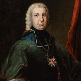 Zdjęcie nr 1: Biskup ukazany do pasa, w trzech czwartych w lewo, z głową zwróconą frontalnie. Jest ubrany w komże i zielony mucet z kapturem i kołnierzem. Na piersi ma zawieszony pektorał, order Orła Białego i gwiazdę orderową. W tle widoczna czerwona kotara. 