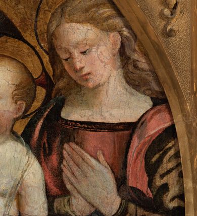 Zdjęcie nr 8: Obraz w formie medalionu w kwadratowej ramie z przedstawieniem Matki Boskiej z Dzieciątkiem oraz dwóch adorujących aniołów. W centrum kompozycji Matka Boska z pochyloną w lewą stronę głową, ukazana jako siedząca, która lewą dłonią przytrzymuje stojące Dzieciątko, a w prawej trzyma chusteczkę. Twarz ma trójkątną o małych oczach i ustach, z długim nosem. Ubrana jest w czerwoną suknię oraz niebieski płaszcz z zieloną podszewką, spięty pod szyją złotą klamrą, zarzucony na głowę i otulający całą postać. Dzieciątko ukazane nagie, zwrócone delikatnie w prawo, lewą rączkę opiera na biodrze, a prawą błogosławi. Twarz ma pełną o rysach dziecięcych, silnie zarumienioną na policzkach, okoloną jasnymi włosami, wokół głowy ma nimb krzyżowy. Po bokach stoją aniołowie, delikatnie pochyleni ku środkowi. Anioł po lewej stronie ma skrzyżowane na piersi ręce. Ubrany jest w żółtą suknię z długimi rękawami oraz niebieską tunikę. Anioł po prawej stronie składa ręce w geście modlitwy. Jets ubrany w brązową suknię z długimi rękawami oraz czerwoną tunikę. Obaj mają delikatne rysy twarzy oraz długie i jasne włosy. Maria oraz aniołowie mają wokół głów koliste nimby nakreślone czarnym konturem. Tło jednolite, złocone. Rama kwadratowa z polem obrazowym w kształcie medalionu, zdobiona na brzegu motywem skręconego sznura, a w przyłuczach stylizowanymi liśćmi akantu. Na odwrociu kartka z drukowanym napisem „Ze zbiorów księdza Jana kniazia z Kozielska Puzyny księcia biskupa krakowskiego, no 11”.
