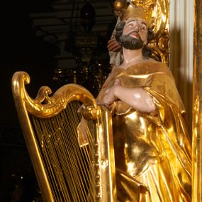 Zdjęcie nr 1: Rzeźba jest drążona z tyłu, ustawiona na niewielkiej, prostej podstawie. Dawid przedstawiony w całej postaci, ukazany jest frontalnie, stoi w kontrapoście, z głową skierowaną w lewą stronę, lekko uniesioną. Jego lewa ręka spoczywa na piersi, prawą przytrzymuje stojącą przed nim harfę. Twarz ma szczupłą, o dużych oczach z głęboko rzeźbionymi powiekami i uniesionymi brwiami, o prostym nosie i pełnych ustach, okoloną krótką kręconą brodą oraz rzeźbionymi w falowane pasma włosami opadającymi na jego lewe ramię. Dawid ubrany jest w wysokie buty, tunikę sięgającą kolan i zbroję torsową, na piersi ma zapięty płaszcz królewski z futrzanym kołnierzem, opadający po bokach postaci i zawinięty na jego prawej nodze. Na głowie ma koronę otwartą. Partie ciała polichromowane naturalistycznie, broda i włosy w kolorze brązowym, zaś części stroju i atrybuty są pozłacane.