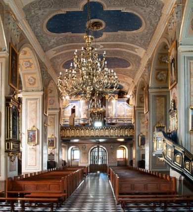 Zdjęcie nr 81: Kościół orientowany, murowany, trzynawowy. Typ halowy, z węższym, prostokątnym prezbiterium zamkniętym trójbocznie oraz z wieżą wbudowaną w zachodnią fasadę. Do prezbiterium od północy przylega zakrystia (do niej od zachodu klatka schodowa wiodąca do skarbca na piętrze), od południa natomiast kaplica Morsztynów z XVII wieku. Kaplica na planie prostokąta zamkniętego trójbocznie, z niszami w ściętych narożach, pod nią sklepiona krypta grobowa, opięta pilastrami wewnątrz i na zewnątrz. Od południa do korpusu przylega kruchta stanowiąca również kaplicę Matki Boskiej Pocieszenia. Korpus czteroprzęsłowy, nawy oddzielają arkady wsparte na filarach, pierwsze stanowią podparcie dla chóru. Nad nawami i prezbiterium strop imitujący sklepienie, na którym malowana dekoracja imitująca gurty, plafony oraz stiuki. Dekoracja ścian powtarza podziały wyznaczone przez arkady, namalowano na nich pilastry podtrzymujące belkowanie. W prezbiterium dwa okna usytuowane niedaleko ołtarza, w nawie osiem, wszystkie w kształcie stojącego prostokąta zamkniętego półkoliście, wypełnione witrażami z dekoracją geometryczną. Główne wejście od zachodu, drugie od północy, trzecie symetrycznie od południa przez kruchtę sklepioną kopułą, kolejne trzy do prezbiterium, od południa przez zakrystię i od północy przez kruchtę. 
Fasada zachodnia na cokole, podzielona gzymsami i lizenami, z wieżą zakończoną hełmem. Na osi drzwi w kształcie stojącego prostokąta flankowane prostokątnymi oknami, powyżej trzecie, większe okno zamknięte łukiem odcinkowym; kondygnację wieńczy gzyms. Druga kondygnacja powtarza podziały pierwszej. W środkowej osi okulus, powyżej dwudzielne okno zamknięte półkoliście. Nad nim tarcza zegara, kolejne dwie na ścianach bocznych. Kondygnacja ograniczona po bokach spływali wolutowymi i obeliskami zakończonymi kulami; przechodzi w wieżę. Powyżej gzyms podtrzymywany kroksztynami. Ostatnia kondygnacja o artykulacji ramowej z balkonami z każdej strony, powyżej wieńczącego gzymsu. Pozostałe elewacje na cokole, kontynuują podziały  lizenowo-ramowe, artykulacją podkreślają okna. Kaplica Morsztynów opięta pilastrami z głowicami, prezbiterium oszkarpowane. Dach nad nawą główną, kaplicą i prezbiterium dwuspadowy, na kruchtą południową kopuła, na wieży ozdobny hełm dołem wklęsły, dekorowany wolutami. Powyżej kopuła, na której latarnia przepruta arkadami i zwieńczona przewężoną w środku kopułą zakończoną ostrosłupem z kulą i krzyżem. 
Do najcenniejszych zabytków świątyni należą m.in. zaprojektowana przez Jana Delamarsa kaplica Morsztynów dekorowana stiukami z 1693 roku autorstwa Baltazara Fontany. Wewnątrz niej warto zwrócić uwagę na osiemnastowieczny ołtarz z przedstawieniem Oblicza Chrystusa i rzeźbionym antepedium. W ołtarz Ukrzyżowania znajdujący się w północnej nawie kościoła wkomponowano gotyckie rzeźby św. Jana i Marii. 