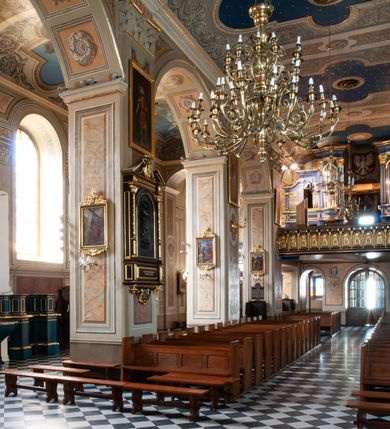 Zdjęcie nr 78: Kościół orientowany, murowany, trzynawowy. Typ halowy, z węższym, prostokątnym prezbiterium zamkniętym trójbocznie oraz z wieżą wbudowaną w zachodnią fasadę. Do prezbiterium od północy przylega zakrystia (do niej od zachodu klatka schodowa wiodąca do skarbca na piętrze), od południa natomiast kaplica Morsztynów z XVII wieku. Kaplica na planie prostokąta zamkniętego trójbocznie, z niszami w ściętych narożach, pod nią sklepiona krypta grobowa, opięta pilastrami wewnątrz i na zewnątrz. Od południa do korpusu przylega kruchta stanowiąca również kaplicę Matki Boskiej Pocieszenia. Korpus czteroprzęsłowy, nawy oddzielają arkady wsparte na filarach, pierwsze stanowią podparcie dla chóru. Nad nawami i prezbiterium strop imitujący sklepienie, na którym malowana dekoracja imitująca gurty, plafony oraz stiuki. Dekoracja ścian powtarza podziały wyznaczone przez arkady, namalowano na nich pilastry podtrzymujące belkowanie. W prezbiterium dwa okna usytuowane niedaleko ołtarza, w nawie osiem, wszystkie w kształcie stojącego prostokąta zamkniętego półkoliście, wypełnione witrażami z dekoracją geometryczną. Główne wejście od zachodu, drugie od północy, trzecie symetrycznie od południa przez kruchtę sklepioną kopułą, kolejne trzy do prezbiterium, od południa przez zakrystię i od północy przez kruchtę. 
Fasada zachodnia na cokole, podzielona gzymsami i lizenami, z wieżą zakończoną hełmem. Na osi drzwi w kształcie stojącego prostokąta flankowane prostokątnymi oknami, powyżej trzecie, większe okno zamknięte łukiem odcinkowym; kondygnację wieńczy gzyms. Druga kondygnacja powtarza podziały pierwszej. W środkowej osi okulus, powyżej dwudzielne okno zamknięte półkoliście. Nad nim tarcza zegara, kolejne dwie na ścianach bocznych. Kondygnacja ograniczona po bokach spływali wolutowymi i obeliskami zakończonymi kulami; przechodzi w wieżę. Powyżej gzyms podtrzymywany kroksztynami. Ostatnia kondygnacja o artykulacji ramowej z balkonami z każdej strony, powyżej wieńczącego gzymsu. Pozostałe elewacje na cokole, kontynuują podziały  lizenowo-ramowe, artykulacją podkreślają okna. Kaplica Morsztynów opięta pilastrami z głowicami, prezbiterium oszkarpowane. Dach nad nawą główną, kaplicą i prezbiterium dwuspadowy, na kruchtą południową kopuła, na wieży ozdobny hełm dołem wklęsły, dekorowany wolutami. Powyżej kopuła, na której latarnia przepruta arkadami i zwieńczona przewężoną w środku kopułą zakończoną ostrosłupem z kulą i krzyżem. 
Do najcenniejszych zabytków świątyni należą m.in. zaprojektowana przez Jana Delamarsa kaplica Morsztynów dekorowana stiukami z 1693 roku autorstwa Baltazara Fontany. Wewnątrz niej warto zwrócić uwagę na osiemnastowieczny ołtarz z przedstawieniem Oblicza Chrystusa i rzeźbionym antepedium. W ołtarz Ukrzyżowania znajdujący się w północnej nawie kościoła wkomponowano gotyckie rzeźby św. Jana i Marii. 