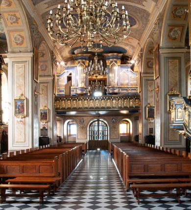 Zdjęcie nr 77: Kościół orientowany, murowany, trzynawowy. Typ halowy, z węższym, prostokątnym prezbiterium zamkniętym trójbocznie oraz z wieżą wbudowaną w zachodnią fasadę. Do prezbiterium od północy przylega zakrystia (do niej od zachodu klatka schodowa wiodąca do skarbca na piętrze), od południa natomiast kaplica Morsztynów z XVII wieku. Kaplica na planie prostokąta zamkniętego trójbocznie, z niszami w ściętych narożach, pod nią sklepiona krypta grobowa, opięta pilastrami wewnątrz i na zewnątrz. Od południa do korpusu przylega kruchta stanowiąca również kaplicę Matki Boskiej Pocieszenia. Korpus czteroprzęsłowy, nawy oddzielają arkady wsparte na filarach, pierwsze stanowią podparcie dla chóru. Nad nawami i prezbiterium strop imitujący sklepienie, na którym malowana dekoracja imitująca gurty, plafony oraz stiuki. Dekoracja ścian powtarza podziały wyznaczone przez arkady, namalowano na nich pilastry podtrzymujące belkowanie. W prezbiterium dwa okna usytuowane niedaleko ołtarza, w nawie osiem, wszystkie w kształcie stojącego prostokąta zamkniętego półkoliście, wypełnione witrażami z dekoracją geometryczną. Główne wejście od zachodu, drugie od północy, trzecie symetrycznie od południa przez kruchtę sklepioną kopułą, kolejne trzy do prezbiterium, od południa przez zakrystię i od północy przez kruchtę. 
Fasada zachodnia na cokole, podzielona gzymsami i lizenami, z wieżą zakończoną hełmem. Na osi drzwi w kształcie stojącego prostokąta flankowane prostokątnymi oknami, powyżej trzecie, większe okno zamknięte łukiem odcinkowym; kondygnację wieńczy gzyms. Druga kondygnacja powtarza podziały pierwszej. W środkowej osi okulus, powyżej dwudzielne okno zamknięte półkoliście. Nad nim tarcza zegara, kolejne dwie na ścianach bocznych. Kondygnacja ograniczona po bokach spływali wolutowymi i obeliskami zakończonymi kulami; przechodzi w wieżę. Powyżej gzyms podtrzymywany kroksztynami. Ostatnia kondygnacja o artykulacji ramowej z balkonami z każdej strony, powyżej wieńczącego gzymsu. Pozostałe elewacje na cokole, kontynuują podziały  lizenowo-ramowe, artykulacją podkreślają okna. Kaplica Morsztynów opięta pilastrami z głowicami, prezbiterium oszkarpowane. Dach nad nawą główną, kaplicą i prezbiterium dwuspadowy, na kruchtą południową kopuła, na wieży ozdobny hełm dołem wklęsły, dekorowany wolutami. Powyżej kopuła, na której latarnia przepruta arkadami i zwieńczona przewężoną w środku kopułą zakończoną ostrosłupem z kulą i krzyżem. 
Do najcenniejszych zabytków świątyni należą m.in. zaprojektowana przez Jana Delamarsa kaplica Morsztynów dekorowana stiukami z 1693 roku autorstwa Baltazara Fontany. Wewnątrz niej warto zwrócić uwagę na osiemnastowieczny ołtarz z przedstawieniem Oblicza Chrystusa i rzeźbionym antepedium. W ołtarz Ukrzyżowania znajdujący się w północnej nawie kościoła wkomponowano gotyckie rzeźby św. Jana i Marii. 